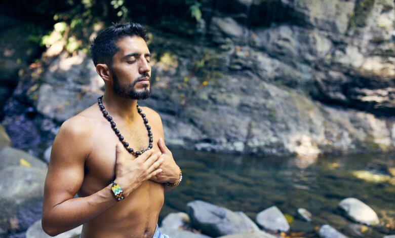 topless man wearing black beaded necklace and blue denim shorts standing on rocky shore during daytime